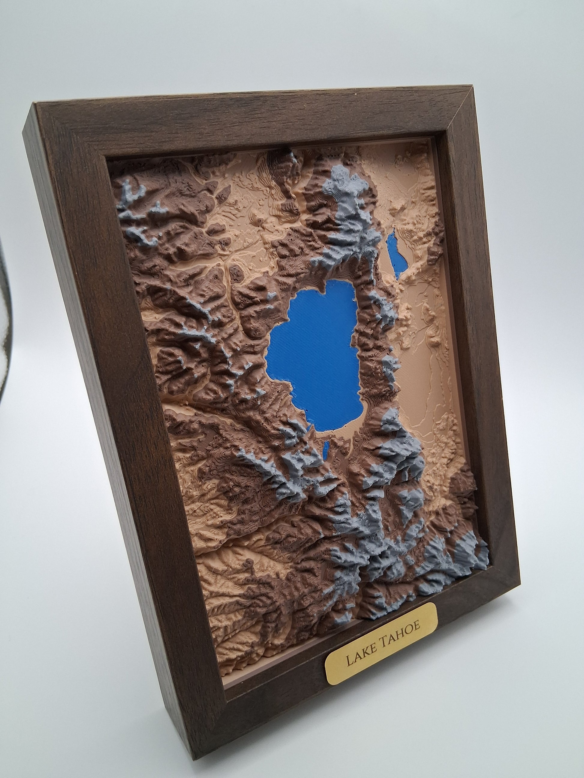 Wooden framed topographic model of a mountainous landscape with a lake, on a white background.