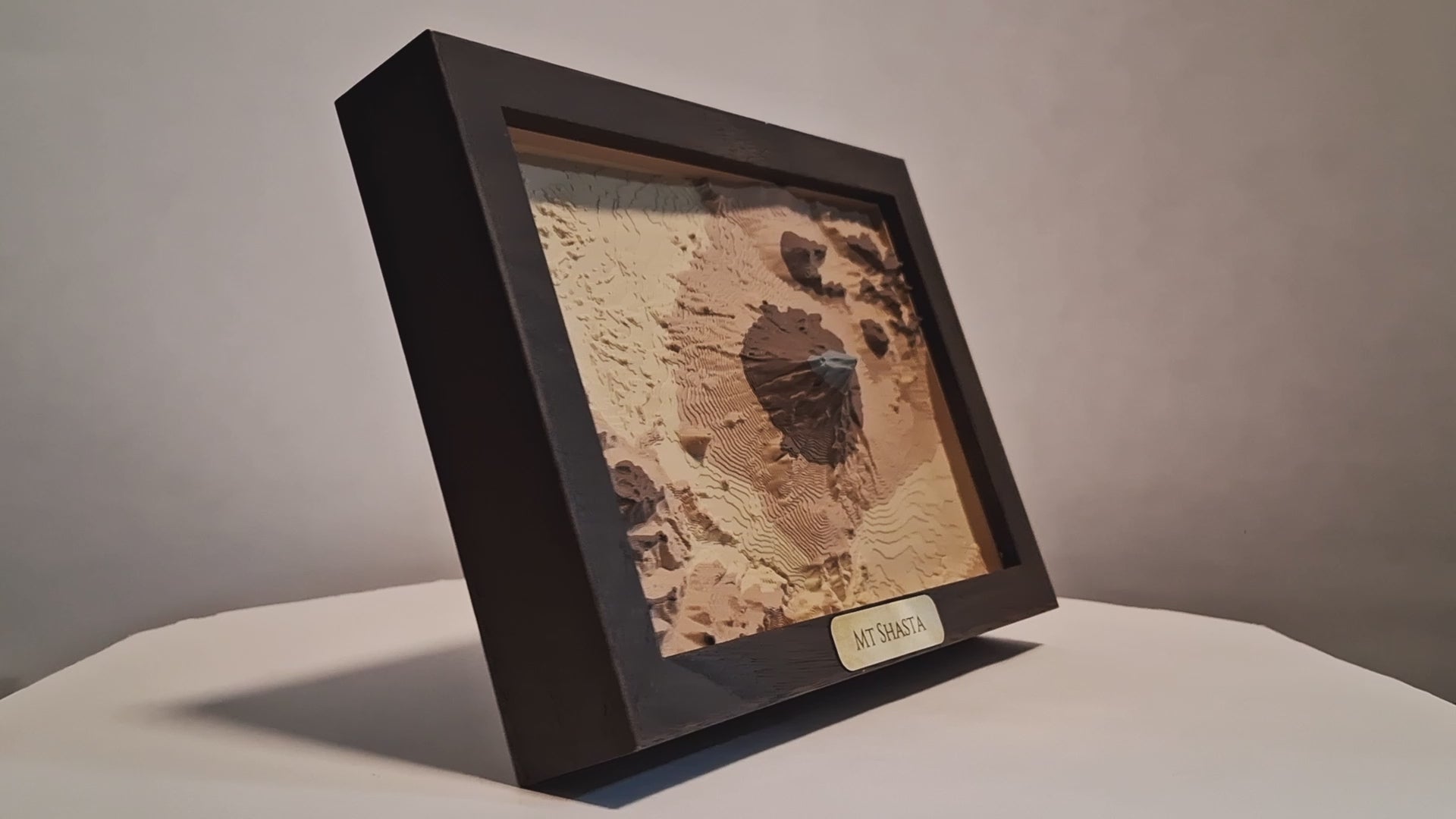 Topographic model of Mount Shasta in a wooden frame on a white background